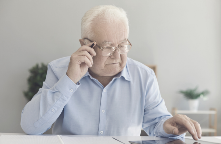 Ein älterer Herr arbeitet am PC und Telefoniert